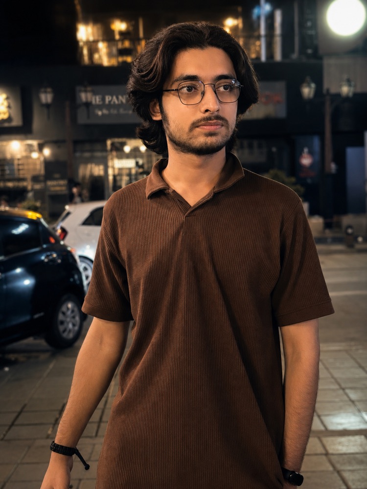 Taqi at night on a lit street, in a brown polo