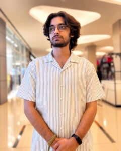 Taqi Saeed in a striped short-sleeve shirt and glasses, standing in a bright shopping mall