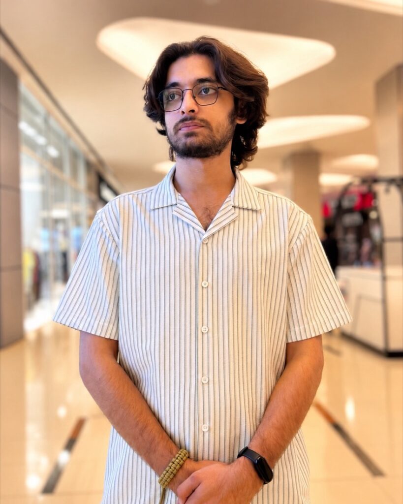 Taqi Saeed in a striped short-sleeve shirt and glasses, standing in a bright shopping mall