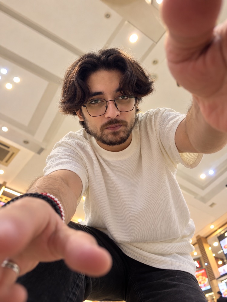Taqi reaching a hand toward the camera, playfully, in a white t-shirt